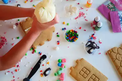 A person decorates gingerbread pieces with icing, surrounded by colorful candies and frosting tools. The activity showcases a fun and creative team-building event, perfect for HR professionals looking to promote collaboration and creativity within their teams.