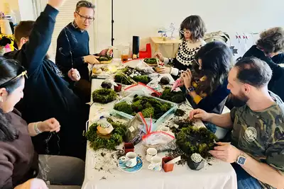 A group of people engaged in a creative team-building activity, sitting around a table and crafting with moss and decorations. They appear focused and collaborative, enjoying an interactive workshop designed for enhancing teamwork skills, ideal for HR professionals planning corporate events.