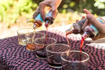 Hands pouring various colorful beverages into glasses for an outdoor team-building event, showcasing an engaging activity perfect for HR professionals looking to foster collaboration and camaraderie among colleagues.