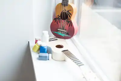 A ukulele on a windowsill next to colorful paint bottles, representing creative team-building activities offered for HR professionals to book for their teams.