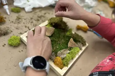 Participant engaging in a team-building workshop, crafting a nature-inspired artwork with moss and small wooden elements, showcasing creative collaboration activities available for booking by HR professionals.