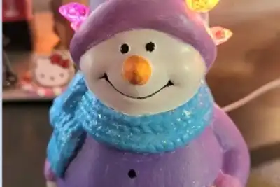 A whimsical snowman figurine wearing a blue scarf and a purple outfit, adorned with colorful holiday lights, perfect for adding a festive touch to team-building events.