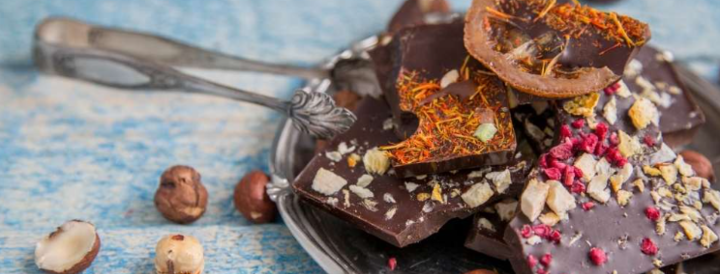 A decorative plate with gourmet chocolate pieces topped with assorted nuts, dried fruits, and spices, ideal for a team-building culinary workshop. Perfect for HR professionals seeking interactive and delicious corporate events.