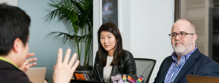 A diverse group of professionals engaged in a lively meeting around a conference table, each with laptops open and actively listening, ideal for promoting teambuilding events for HR professionals seeking to enhance collaboration and communication skills within their teams.