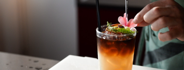 A person garnishing a cocktail with a pink flower, representing a creative and engaging workshop offered as part of a team-building event for HR professionals.