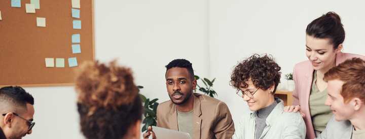 A diverse group of colleagues engaged in a collaborative team meeting, discussing ideas and working together at a table with laptops and documents, capturing the essence of productive teambuilding activities.