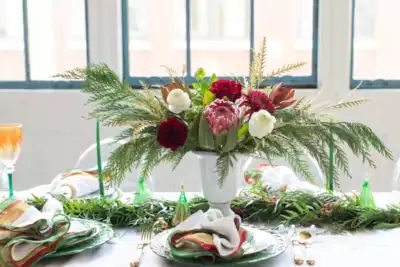 Elegant table setting ideal for team-building events, featuring a centerpiece of lush greenery and vibrant flowers in red and white, surrounded by green-tinted glassware and neatly folded napkins. Perfect ambiance for HR professionals booking memorable gatherings.