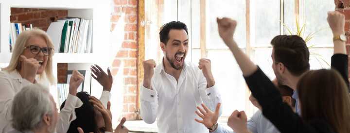 A diverse group of colleagues enthusiastically cheering and celebrating in a bright office setting, illustrating the success of a team-building activity.